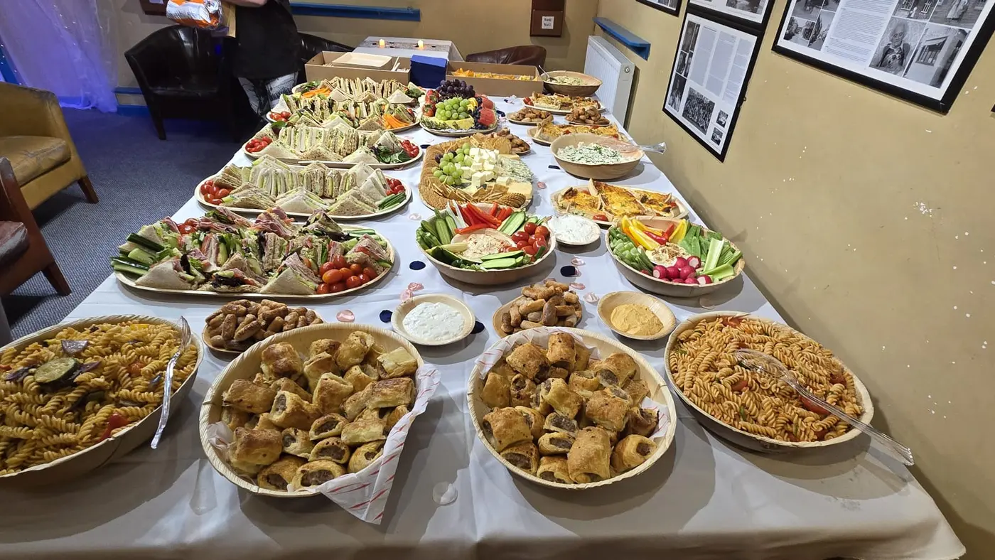 A long table laden with a variety of buffet food including sandwiches, sausage rolls, and salads.