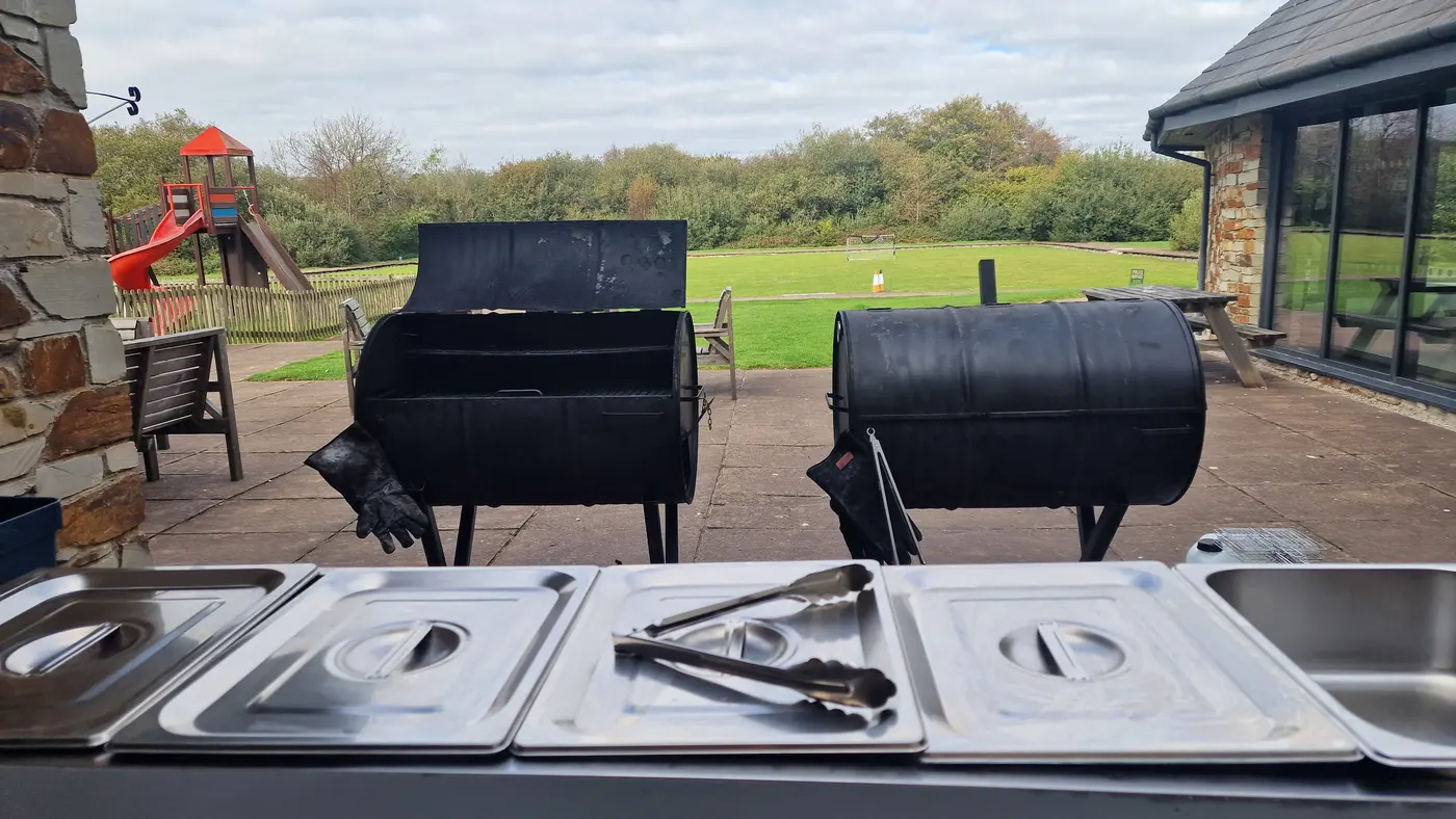 Two large barrel smokers stand ready on a patio with serving trays in the foreground.