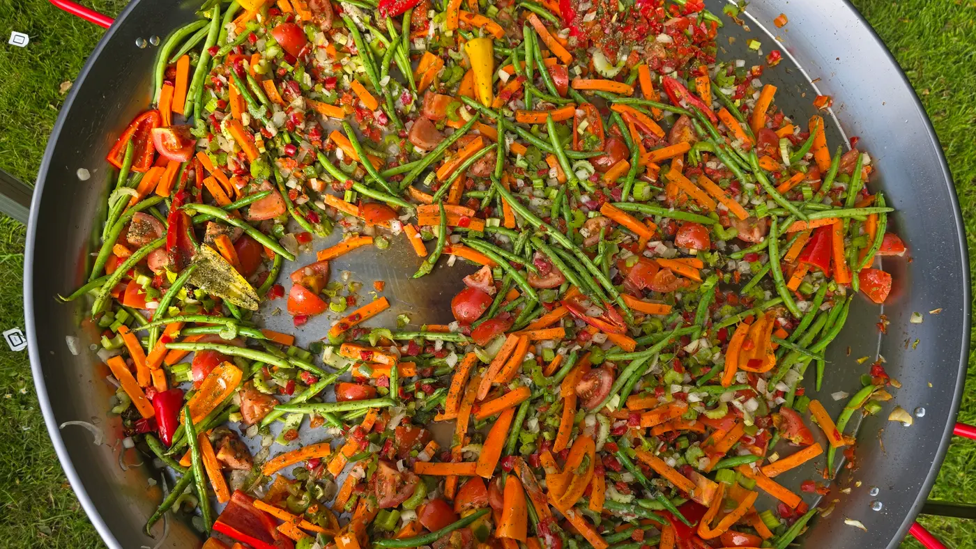 A giant paella pan filled with fresh, colourful vegetables ready for cooking.