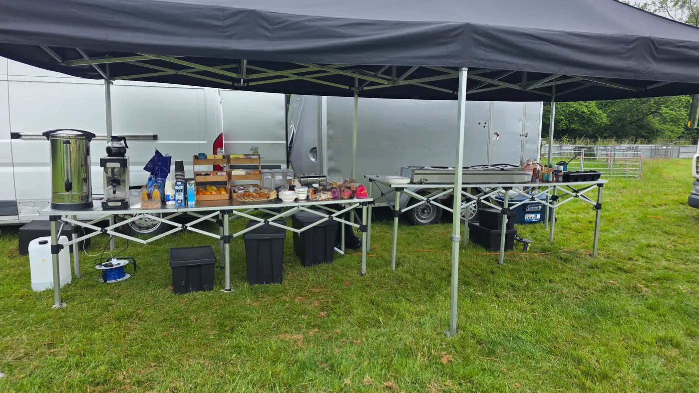 Outdoor catering setup with a tent, tables, food, and drinks.