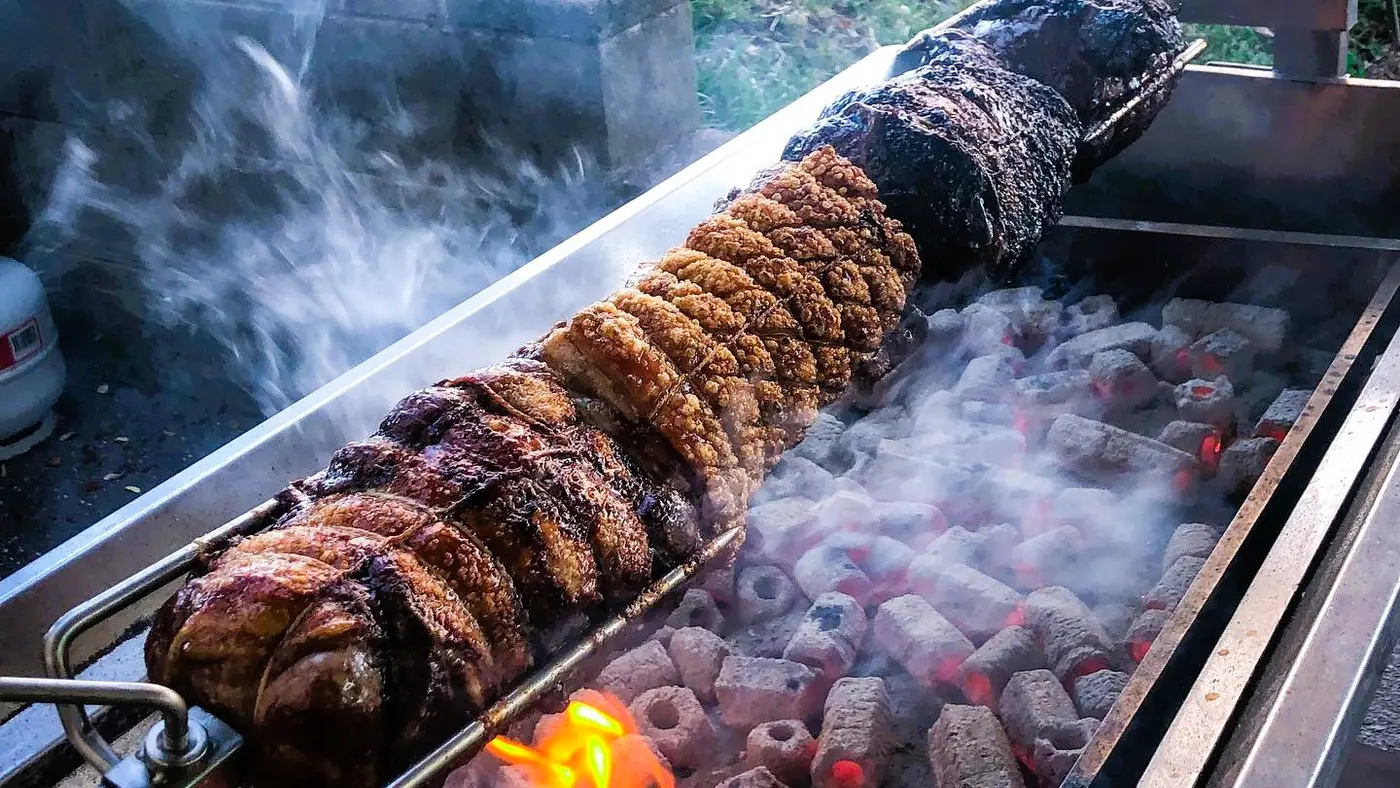 A large hog roast is slowly rotating over glowing coals and open flames.