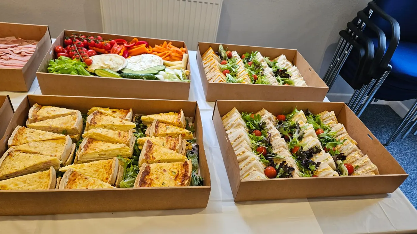 Assortment of catering boxes filled with sandwiches, quiches, and vegetable platters.