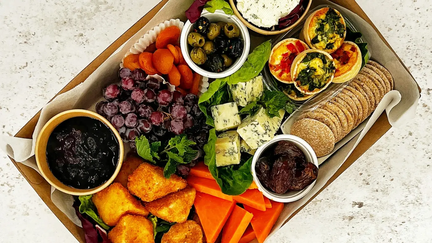 A delicious platter of cheese, crackers, fruit, olives, and mini quiches.