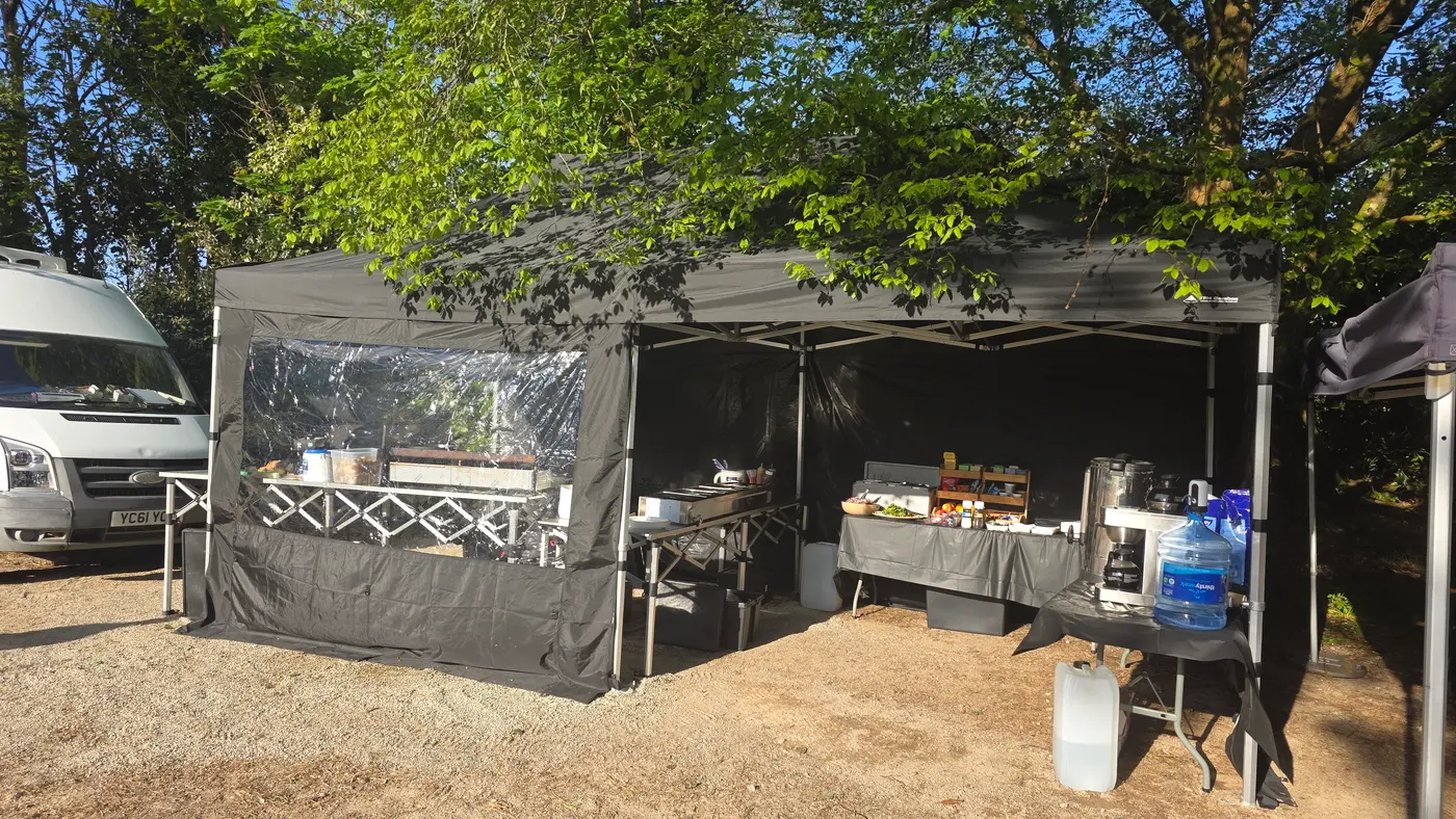 An outdoor catering setup with a tent, tables, and a van in the background.