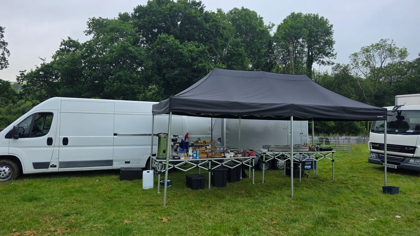 Outdoor catering setup with vans, a tent, and tables displaying food items.