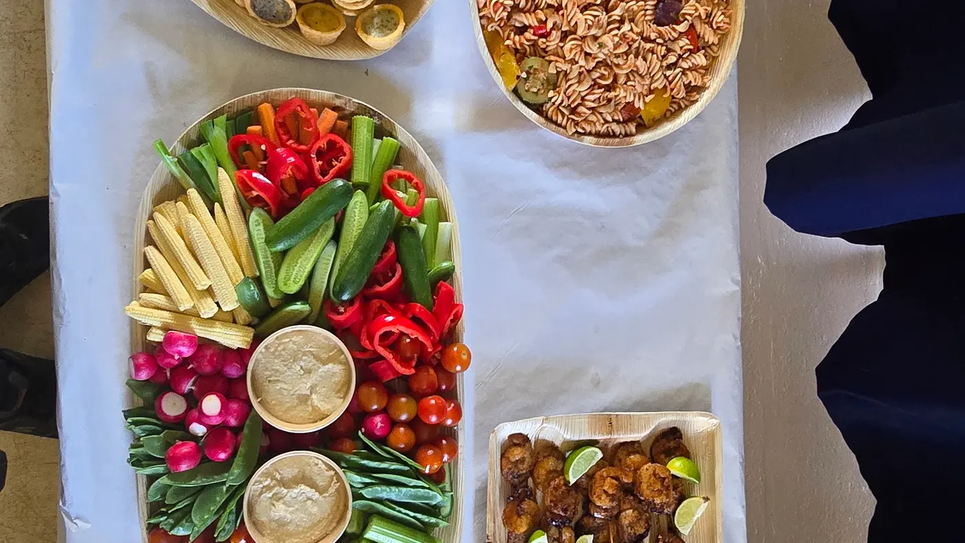 A long table displays a variety of buffet dishes including salads, bread, and skewers.