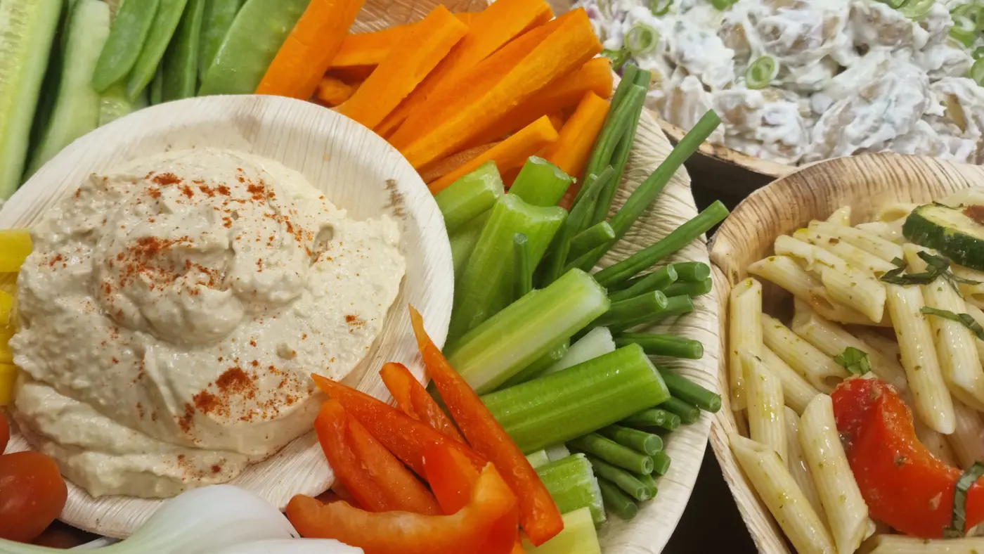 A selection of fresh vegetable crudités, hummus, pasta salad, and potato salad.