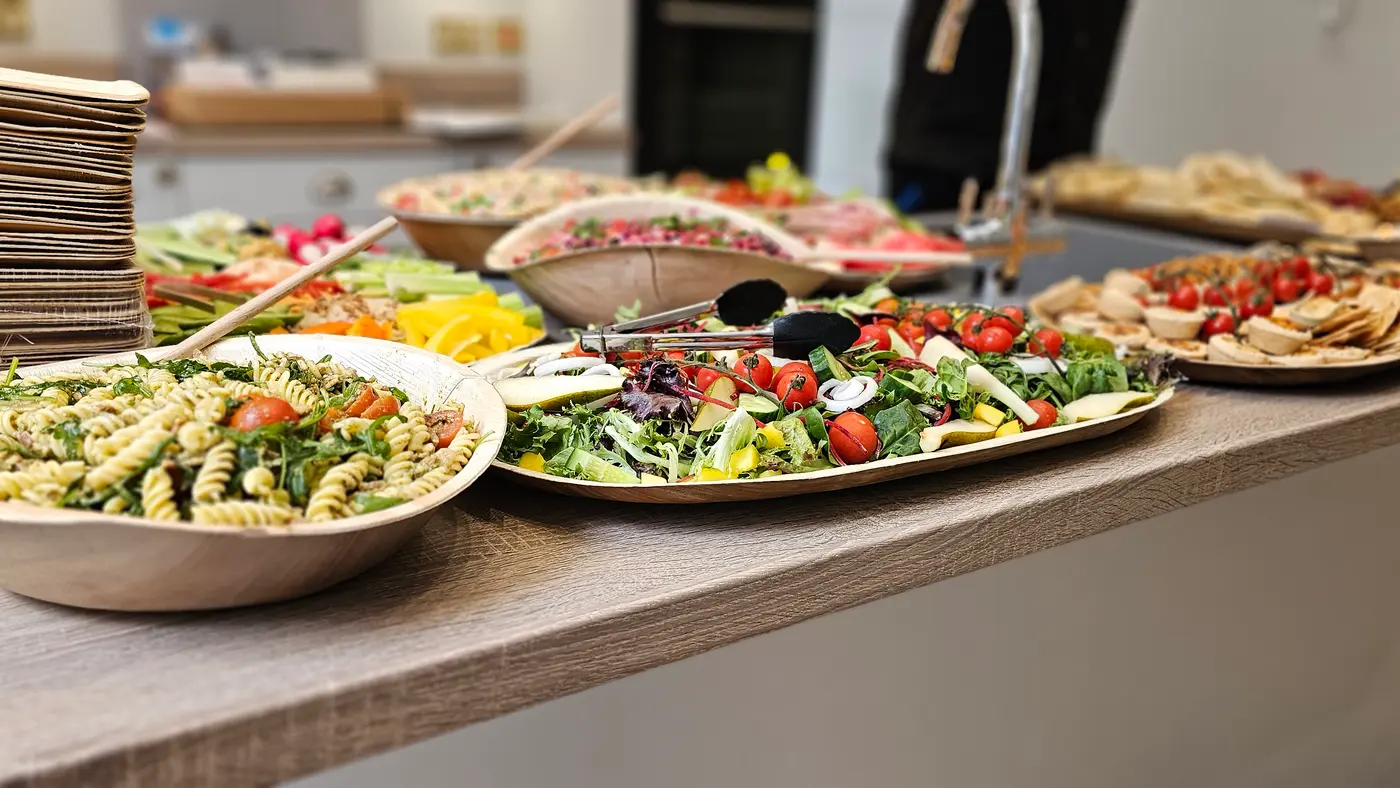 A spread of fresh salads, pasta salad, and appetizers laid out on a counter.