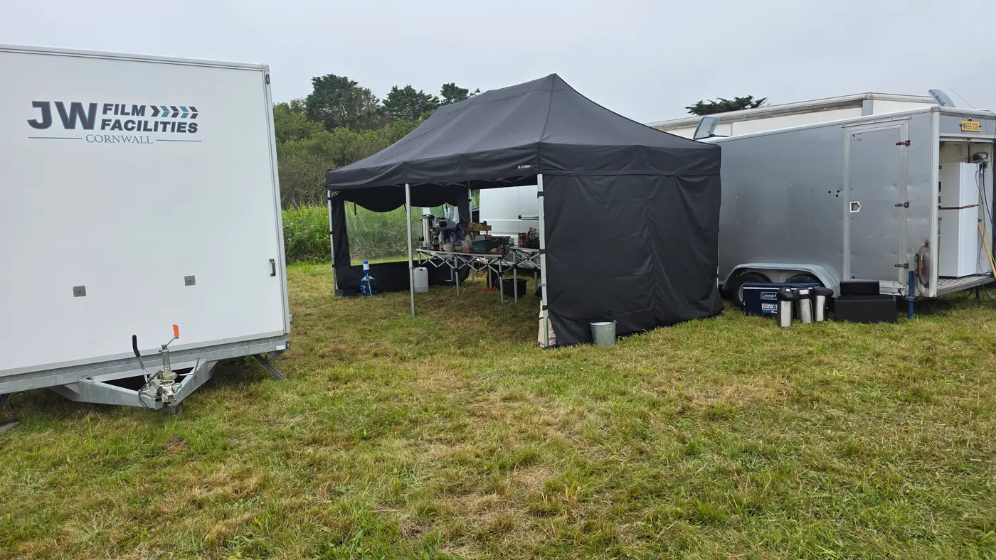 Outdoor catering setup with trailers and a black tent on a grassy field.