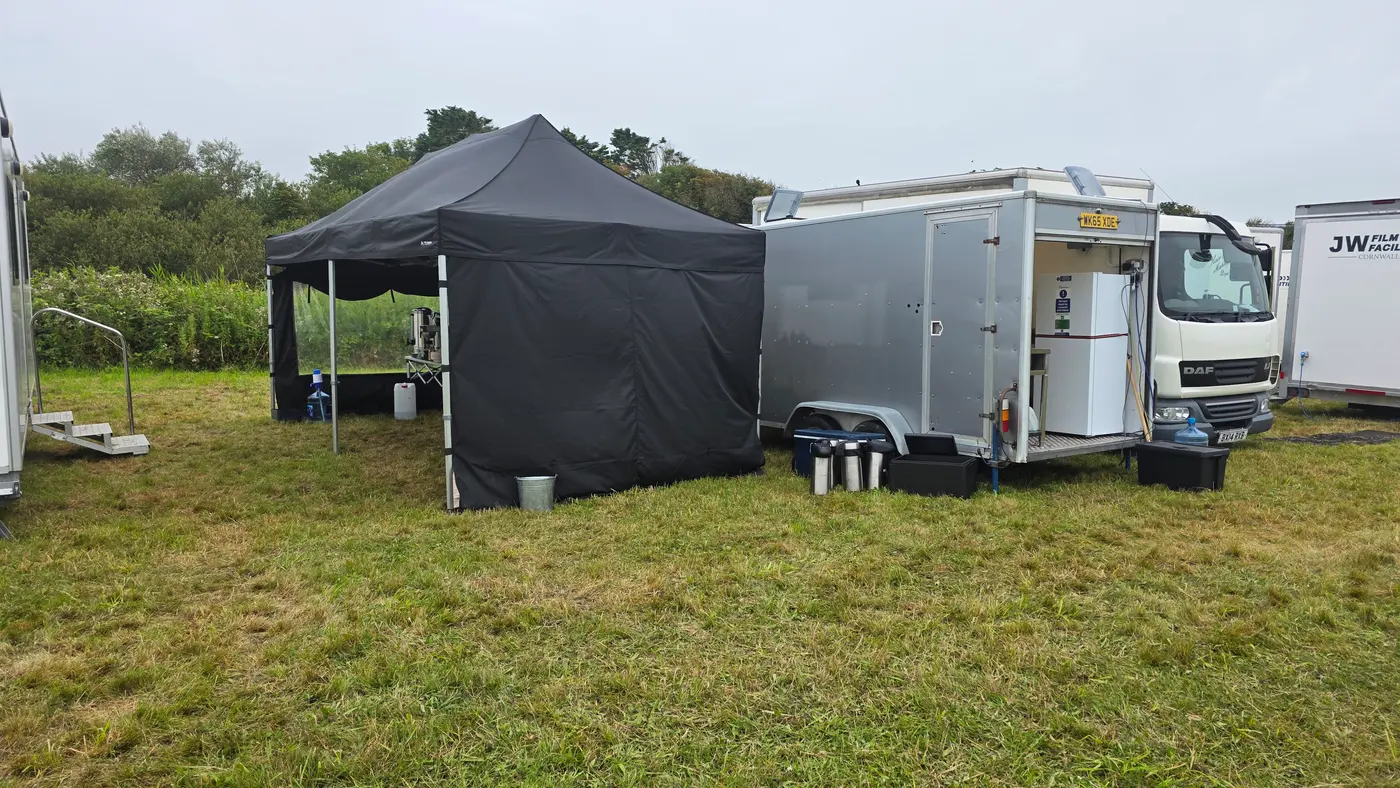 Outdoor catering unit setup with a tent, trailer, and truck on a grassy field.