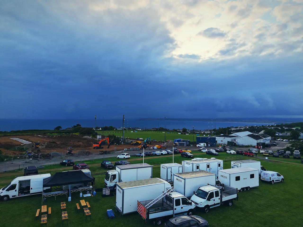 Aerial of a complete film unit base above St Ives Bay, Cornwall — Salt Wind catering gazebo with JW Film Facilities trailers under a storm sky