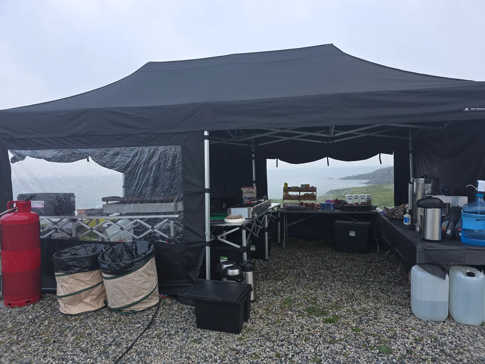 Salt Wind Catering gazebo pitched on a Cornish clifftop in sea mist — gas, urns and water carried in, no mains power on site
