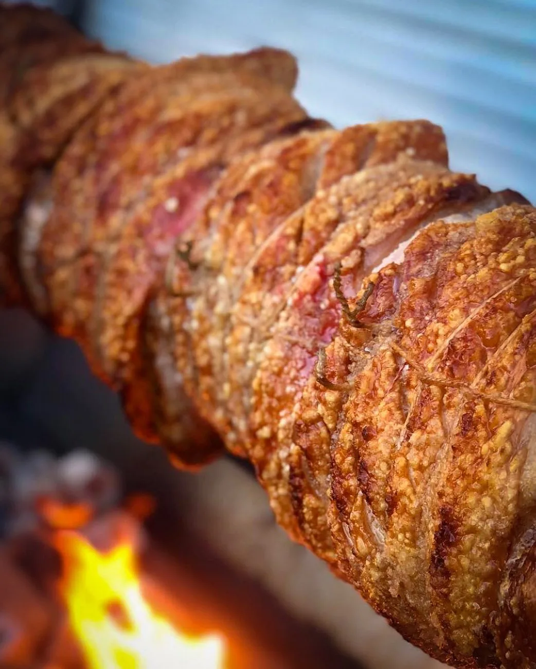 Close-up of crispy golden hog crackling turning on the spit over open flame
