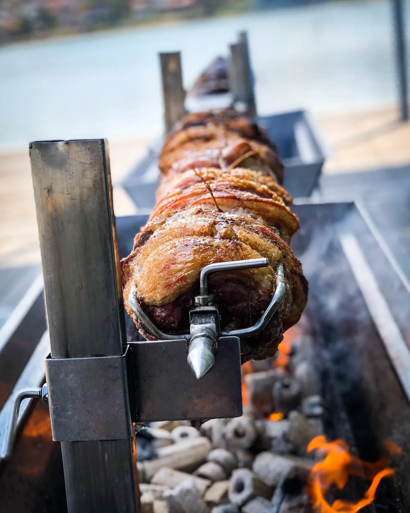 Whole hog roasting on a spit over glowing coals with the Cornish coast in the background